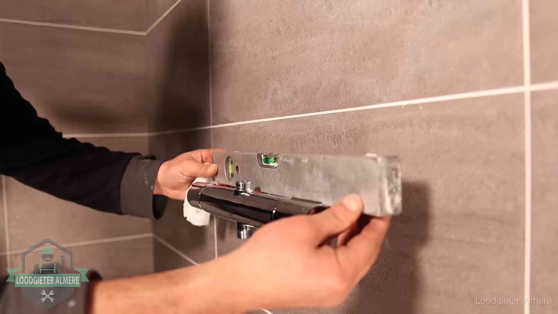 Loodgieter lijnt een douchekraan uit met een waterpas in een woning in Almere