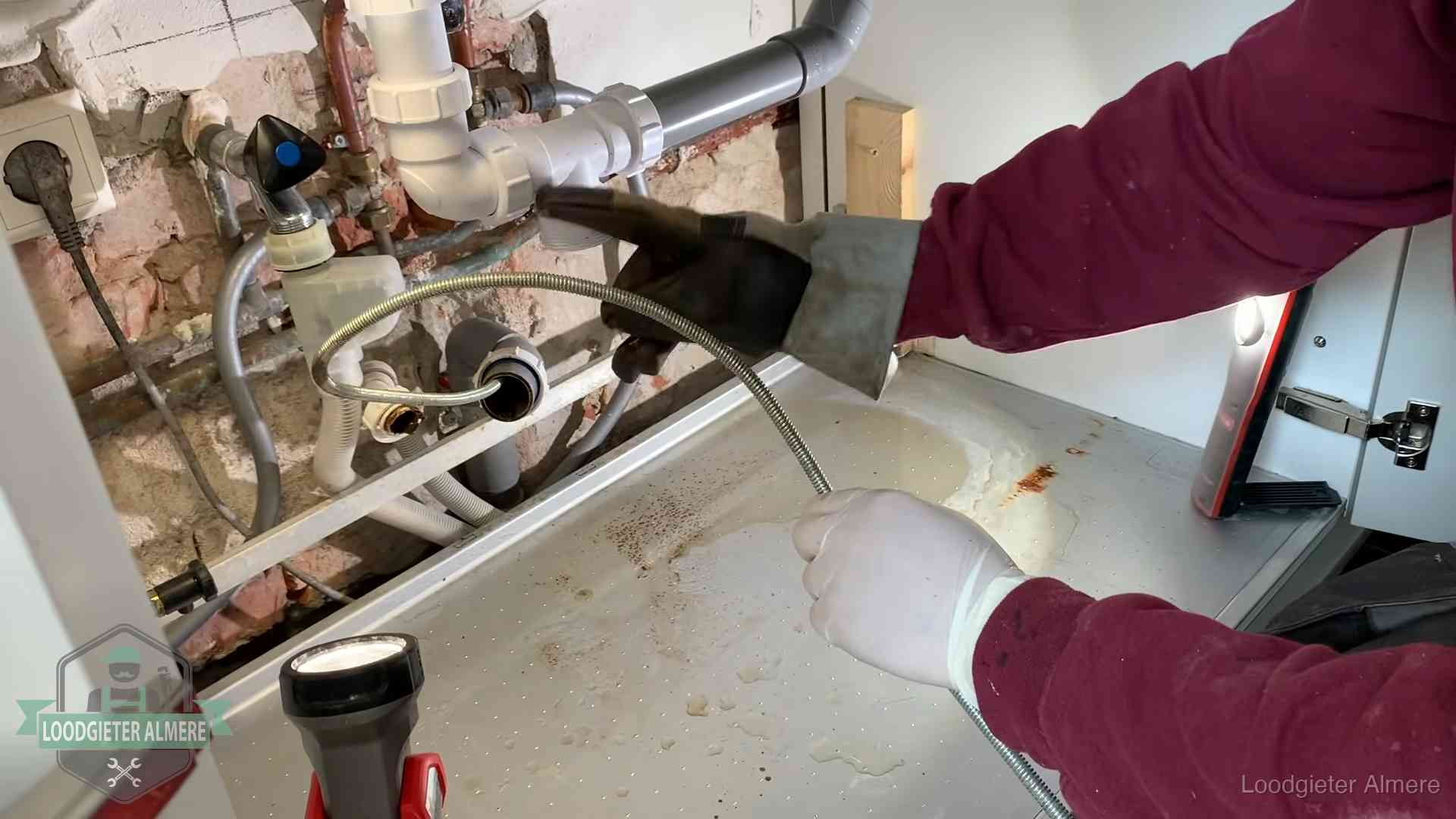 Ontstoppingsveer gaat in een geopende sifonaansluiting onder het aanrecht in Almere