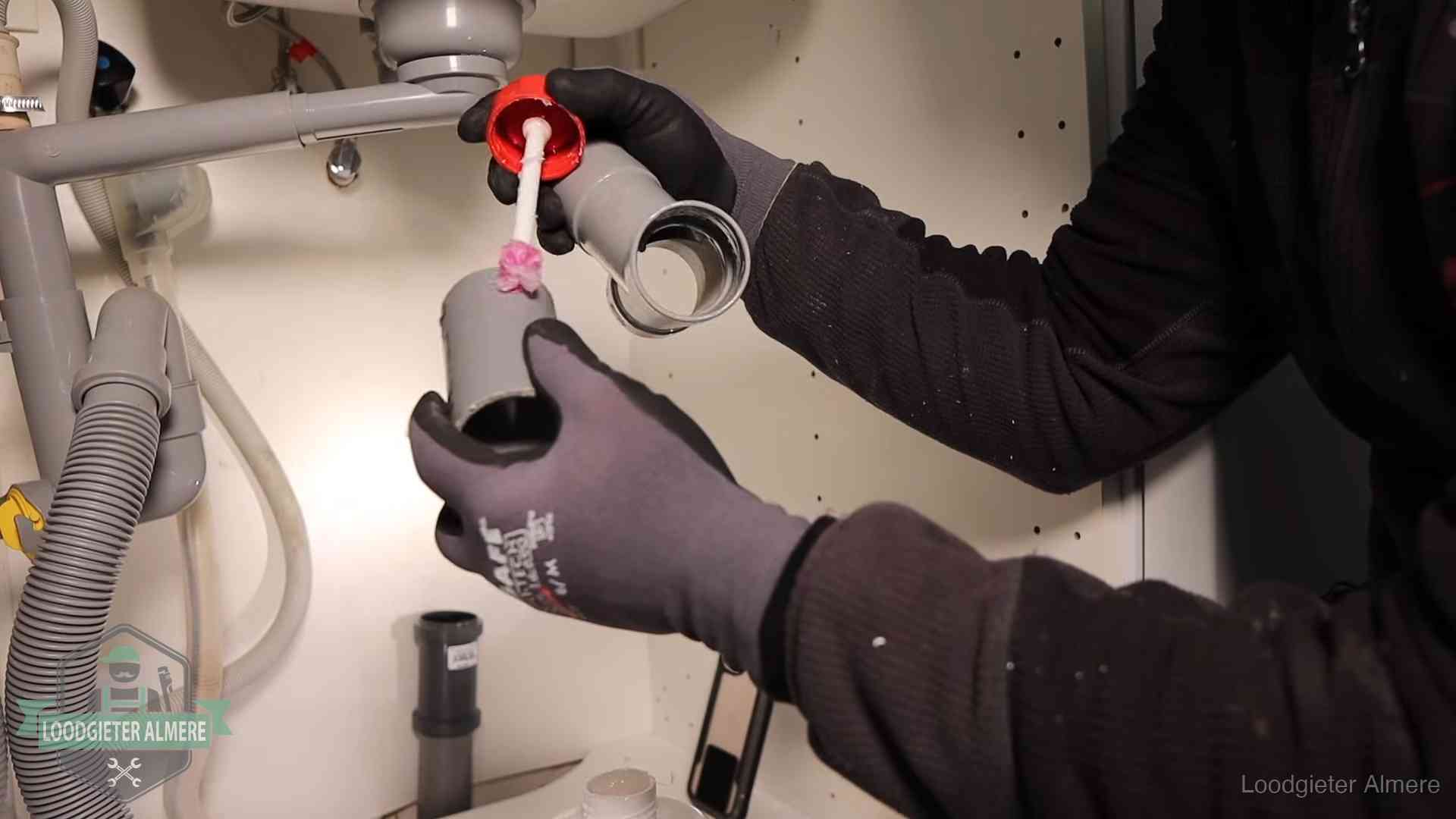Loodgieter demonteert en reinigt de sifon onder een keukenkast in Almere