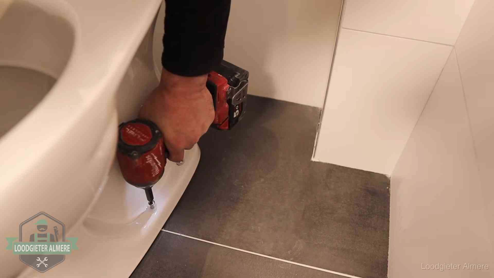 Kosten wc ontstoppen in Almere Loodgieter zet de voet van een wc-pot vast op de tegelvloer in Almere